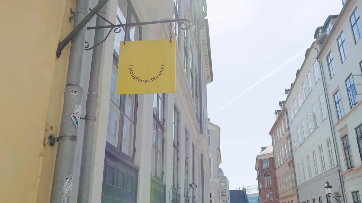路地に吊るされた黄色い看板に「The Happiness Museum」の文字と笑顔のマーク