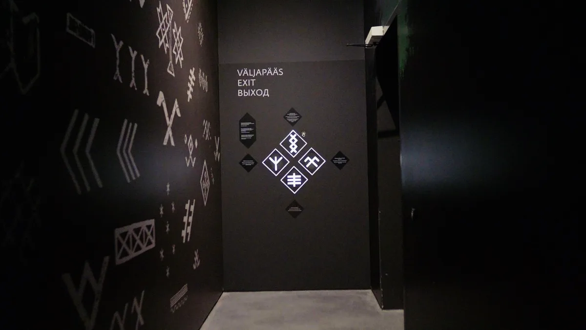 黒い壁に白い模様が描かれた出口。扉に4つのマークのボタンがある