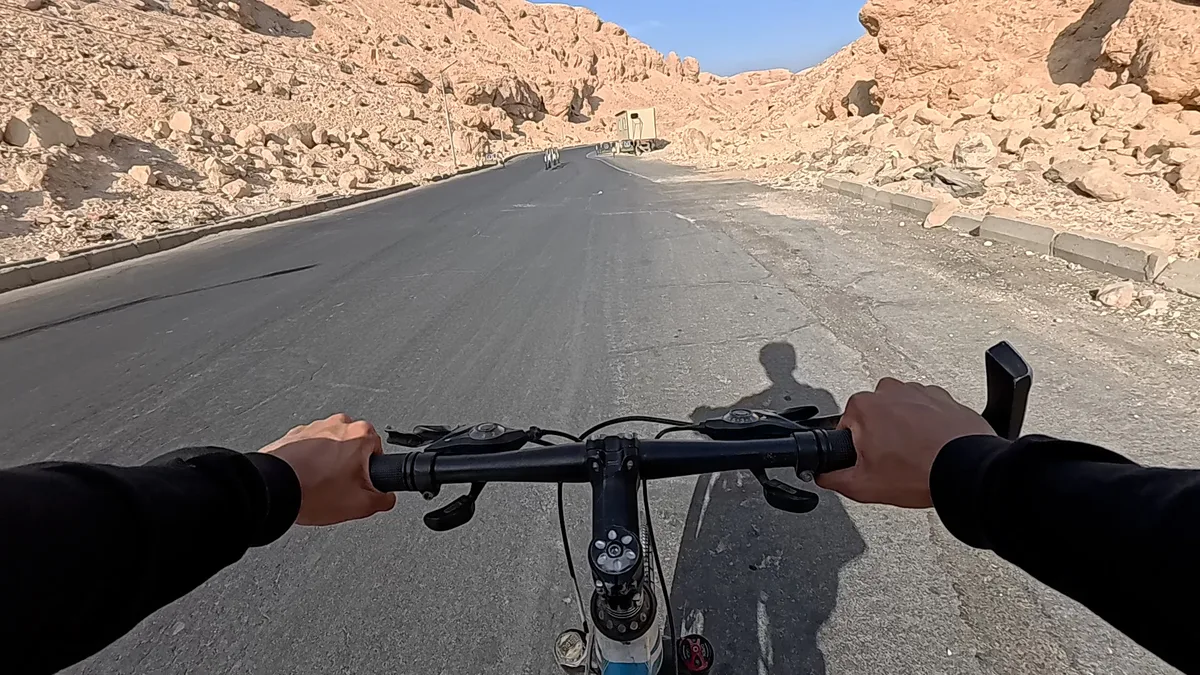 自転車のハンドル越しに見た舗装路。両脇は乾いた岩山が続く