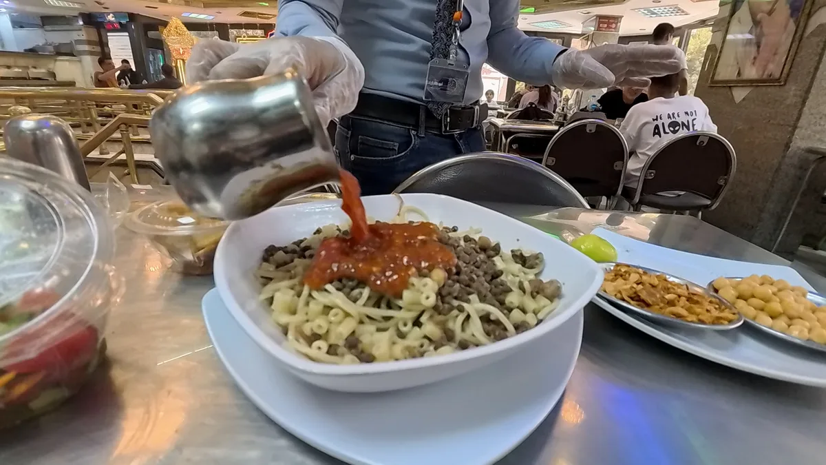 屋台でコシャリにトマトソースをかけているところ。米とマカロニとレンズ豆を重ねた一皿