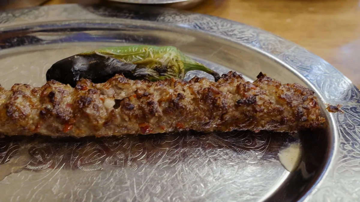 銀色の皿に盛られた串焼きの挽き肉ケバブと、焼いた青唐辛子